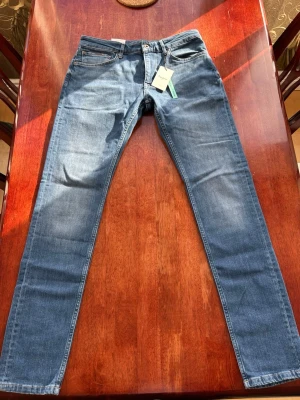 Blå tapered jeans från Pepe Jeans - Säljer ett par klassiska blå tapered jeans från Pepe Jeans London. Jeansen har normalhög midja, raka ben och är tillverkade i slitstarkt denim. Snygg läderpatch med logga baktill i midjan. Perfekta för en avslappnad och trendig look. 32W 34L