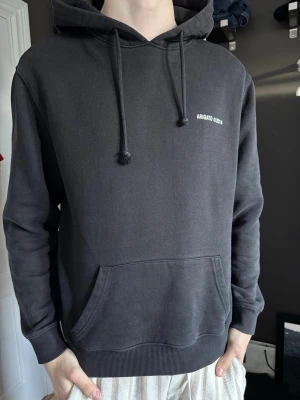 Svart hoodie från Axel Arigato - Svart hoodie från Axel Arigato med vit text 'ARIGATO ©2014' på bröstet och ryggen. Klassisk känguruficka framtill, ribbade muddar och justerbar huva med dragsko. Perfekt för en chill och stilren look.