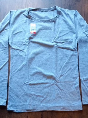 1 stycken ljusgrå långärmade tröja till barn 5 år - 1 stycken ljusgrå långärmade tröja till barn 5 år i mjukt och stretchigt material. Enkel och stilren design med rund halsringning. Perfekt för lager-på-lager och chill dagar. Tröjan har ingen synlig logga eller tryck på framsidan.
