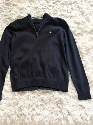 Mörkblå half zip tröja från Gant - Klassisk svart långärmad tröja från Gant med half zip och liten broderad logga på bröstet. Tröjan har en stilren design och är tillverkad i mjuk bomull, perfekt för en avslappnad men snygg look.