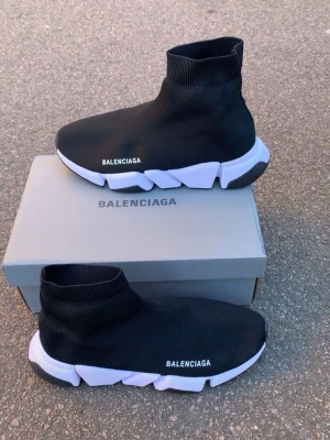 Balenciaga Speed Trainer sneakers svart/vit - Balenciaga Speed Trainer sneakers i svart stretchig textil med vit chunky sula och logga på sidan. Strumpliknande design som sitter tight runt ankeln och ger en futuristisk vibe. Sulan är grov och har svarta detaljer undertill för extra grepp.