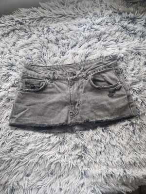 Grå minikjol med slitningar - Trendig kjol i denim med råa kanter och slitna detaljer framtill och baktill. Klassisk femficksmodell med knapp och dragkedja. Perfekt för en avslappnad streetstyle-look. mått finns på sista bilden❤️