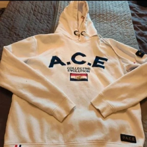 Vit hoodie från A.C.E Collective Evolution - Vit hoodie från A.C.E Collective Evolution XL  Vit hoodie från A.C.E Collective Evolution med broderad logga och text i mörkblått på bröstet. Tröjan har huva med snörning, ribbade muddar och detaljer i rött, vitt och blått. Snygg patch på ärmen och nertill. Perfekt för dig som gillar streetwear.  Osäker på om det är herr eller dam storlek. Tror herr !!!!Liten i storlek!!!!!!  Kan även hämtas I Partille  E1