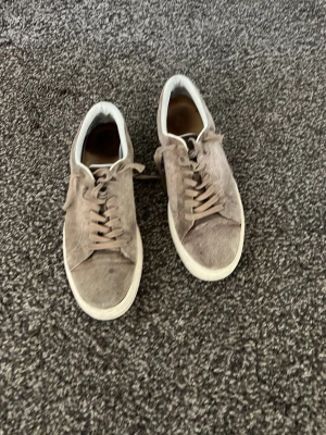 Beige mockasneakers med vit sula - Snygga sneakers i beige mocka med klassisk låg profil och vita sulor. Skorna har matchande beige snörning och en stilren design som passar till det mesta. Perfekta för dig som gillar en clean och enkel look.