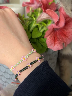 Handgjorda blomarmband  - Handgjorda blomarmband.  Bestäm färg på blomma, tråd och om du vill ha ljus- eller mörkgrön färg på ”bladen” runt om.  5kr skänks till Barncancerfonden för varje sålt armband🎗️   Färger till blomma: - röd - rosa (3 olika varianter) - blå (3olika varianter) - ljusblå - lila - peach  - guld - vit - svart - grå