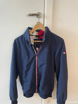 Marinblå vindjacka Tommy Hilfiger - Tja, säljer denna snygga marinblå vindjacka från Tommy Hilfiger med dragkedja framtill. Storlek 176 stor S eller liten M kan ochså har den skicket är 9/10 😊👍🏼 vid mer bilder eller frågor hojta bara till 😌