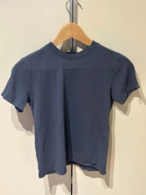 Blå basic t-shirt med kort ärm 146/152 - En enkel blå t-shirt i mjuk bomull med rund halsringning och korta ärmar. Perfekt till jeans eller shorts för en clean och avslappnad look. Klassisk passform utan tryck eller mönster.