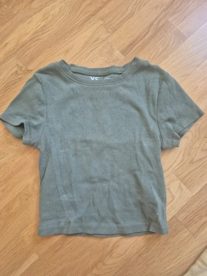 Olivgrön ribbad kortärmad topp - En enkel och stilren olivgrön topp med ribbad struktur och korta ärmar. Modellen är croppad och har en rund halsringning. 