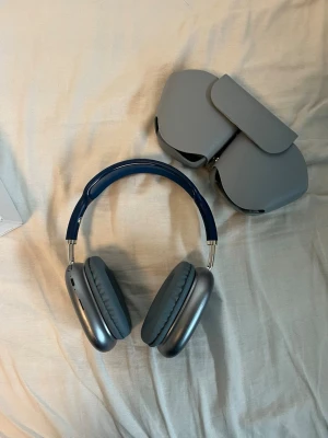 Airpods max - Snygga over-ear hörlurar i blått och silver med mjuka öronkuddar och justerbart huvudband. Hörlurarna har en modern design med metalliska kåpor och följer med ett matchande grått fodral. Perfekta för musik, gaming eller film.
