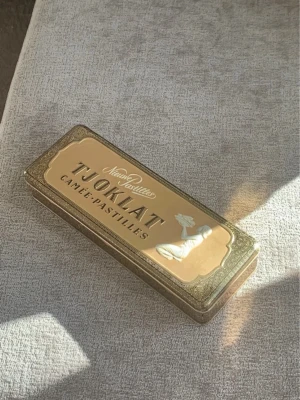 Antik chokladask  - Säljer en retro plåtask från Tjoklat med guldfärgad design och dekorativt mönster. Locket har texten 'Cameé-Pastilles' och en elegant illustration. Perfekt som samlarobjekt eller för förvaring av småsaker.