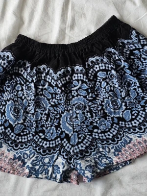 Oanvända mönstrade boho-shorts,elastisk midja ☀️ - Svala och jättesköna sommarshorts med fint mönster i blått, svart och vitt, köpta på Cypern. Modellen är väldigt kort och har en bekväm resår i midjan. Shortsen är helt oanvända, endast tvättade en gång efter inköp, så de är i absolut nyskick!Lappen säger ”Standard Size”, men de passar och upplevs bäst som en XS eller en mindre S då de är väldigt korta. Se exakta mått nedan.          Midjehöjd: 28 cm       Midjemått: 27 cm x 2 (töjs ut mycket tack vare resåren)Innerbensmått: 5 cm