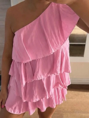 Rosa one shoulder volangklänning - Söt rosa kortklänning med one shoulder-design och flera volanglager. Xs/s helt ny prislappen kvar aldrig använd behöver få såld snabbt