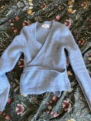 Ljusblå omlottkofta från Gina Tricot - Mysig ljusblå stickad omlottkofta från Gina Tricot i ullblandning. Koftan har långa ärmar, ribbade muddar och knytskärp i midjan för en snygg siluett. Perfekt för lager på lager och en chill look. Använd 2 gånger, nytt skick!🩵🩵 nypris 400kr!