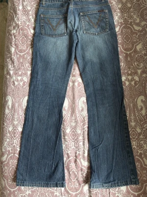Blå straight jeans med fickdetaljer  - Säljer ett par klassiska blå bootcut jeans med snygga fickdetaljer bak. Jeansen har en lätt tvättad look och raka ben som går ut något nedtill. Perfekta till sneakers eller boots och gjorda i mjukt denimtyg.