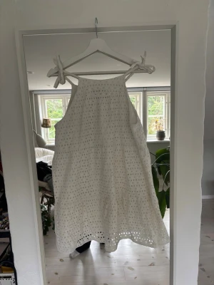 Vit somrig klänning med knytband - Står att den är L men sitter som en S!!! Superfin vit klänning i bomull med broderade detaljer och knytband på axlarna. Klänningen är ärmlös, har en luftig passform och är perfekt för varma dagar. Den har en kort längd och ett romantiskt uttryck med spetsliknande mönster. 