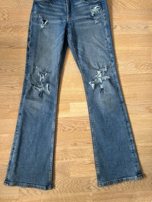 Blå slitna bootcut jeans - Säljer ett par blå bootcut jeans med slitningar och hål på låren och knäna. De har använts några gånger och pris kan diskuteras