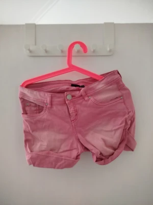 Rosa shorts med fem fickor - Snygga rosa shorts med klassisk femficksdesign och uppvikta benslut. De har knapp och dragkedja framtill samt bälteshällor i midjan. Perfekta för varma dagar och ger en fräsch look till din outfit.