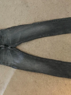 Grå  jeans med raka ben - Säljer ett par grå jeans med slitningar och raka ben. Jeansen har klassisk femficksmodell och kontrastsömmar. Baktill finns två fickor med dekorativa sömmar. Perfekta för en avslappnad och trendig look.