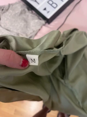 Ljusgrön satinmorgonrock M - Snygg ljusgrön morgonrock i glansigt satinmaterial. Modellen har trekvartsärmar och ett matchande midjeband för att knyta i midjan. Perfekt för att chilla hemma i och ger en lyxig känsla till din loungewear.