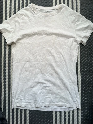 Vit basic t-shirt från 157 - En enkel vit t-shirt från 157 med rund hals och korta ärmar. Tillverkad i mjuk bomull som känns skön mot huden. Perfekt att matcha med jeans eller shorts för en clean och avslappnad stil.