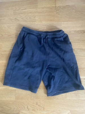 Mörkblå bomullsshorts med snörning - Säljer ett par mörkblå shorts i mjuk bomull med elastisk midja och snörning framtill. Shortsen har en avslappnad passform och sidofickor, perfekta för chill dagar eller träning.