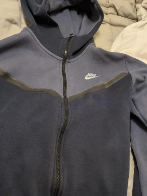 Blå zip hoodie från Nike - Snygg blå hoodie från Nike med dragkedja framtill och huva. Har en diskret grå detalj över bröstet och Nike-logga på vänster sida. Perfekt för chill dagar eller när du vill ha en sportig look. Mjuk och skön bomullsblandning.
