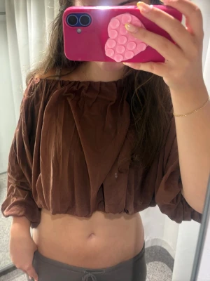 Populär brun topp hm - Säljer en brun croppad blus med ballongärmar och lös passform. Toppen har en offshoulder-design och är gjord i ett mjukt, tunt tyg som ger en avslappnad vibe. Perfekt för dig som gillar trendiga och bekväma plagg. Storleken på denna topp är L men jag på bilden bär vanligtvis S/xs i toppar. Helt ny!!!!🤎🤎
