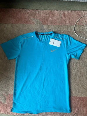Nike t-shirt  - Tränings t-shirt från Nike Running. Tröjan är designad för löpning och har en bekväm passform. Den är i en ljusblå nyans med reflekterande detaljer på axlarna och en silverfärgad Nike-logotyp på bröstet. Etiketten "NIKE RUNNING" syns tydligt i nacken. Köpt i Nike butik, men blev till aldrig någon användning. Pris kan diskuteras!!