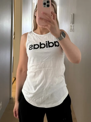 Vit ärmlös topp från Adidas - Snygg vit ärmlös topp från Adidas med svart logga framtill. Oversized 