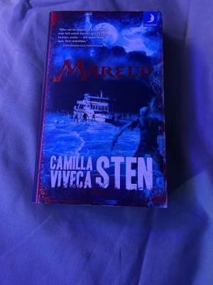 Mareld av Camilla och Viveca Sten - En spännande skönlitterär bok med titeln 'Mareld' av Camilla och Viveca Sten. Omslaget är blått med dramatiska illustrationer av is, vatten och en färja. Boken är i pocketformat och tillhör serien Havsfolket.