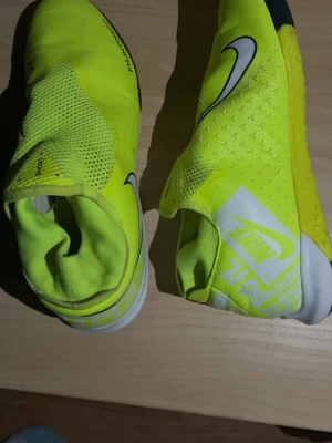 Nike Phantom Vision gula inomhus fotbollsskor - Säljer ett par Nike Phantom inomhus fotbollsskor i neon-gult med svart och vitt. Skorna har en strumpliknande passform med snörning, meshdetaljer och slitstark sula för inomhusspel. Stora Nike-loggor på sidan och hälen. Perfekta för dig som vill sticka ut på planen. Pris kan diskuteras.