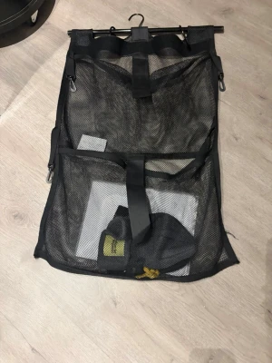 Svart mesh organiseringsväska - Praktisk svart organiseringsväska i mesh med flera fack och remmar. Perfekt för att hålla ordning på småprylar eller kläder. Väskan har en krok upptill för enkel upphängning och är lätt att ta med sig. Skriv ifall du vill ha mer info osv inklusive pris.