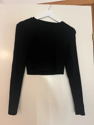 Svart croppad långärmad topp Gina Tricot - Säljer en svart croppad långärmad topp från Gina Tricot. Enkel och stilren design med rund halsringning och tight passform. 95% bomull