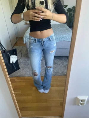 Ljusblå slitna bootcut jeans - Säljer ett par ljusblå bootcut jeans med slitningar och hål på låren och knäna. Jeansen har låg midja, klassiska fem fickor och är i ett mjukt denimtyg. Perfekta för en avslappnad och trendig look. Dom är i längden Tall 