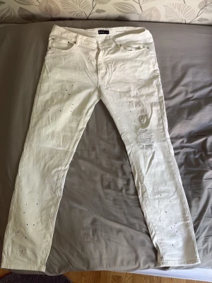 Vita slitna Purple jeans - Säljer ett par oanvända vita purple jeans med skinny fit och slitningar samt hål på benen för en trendig look. Jeansen har fem fickor och detaljerade slitningar på framsidan.