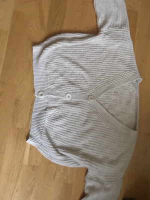 Beige ribbstickad kofta med knappar - Snygg beige ribbstickad kofta med v-ringning och tre knappar framtill. Koftan har långa ärmar och är gjord i ett mjukt, tunt material som passar perfekt till lager-på-lager. Enkel och stilren design som funkar till det mesta.