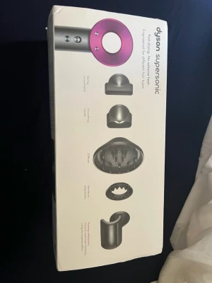 Dyson Supersonic hårfön - Säljer en Dyson Supersonic hårfön i silver och rosa. Medföljer flera munstycken för styling, utjämning, diffuser och koncentrator. Modern design och kraftfull motor, perfekt för olika hårtyper. Instruktionshäfte ingår.