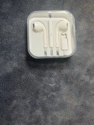 Earphones  - Säljer ett par vita EarPhoned med Lightning-kontakt. Klassisk design med inbyggd fjärrkontroll och mikrofon på sladden. Kommer i original plastetui. Perfekt för dig som vill ha trådade hörlurar till din iPhone.