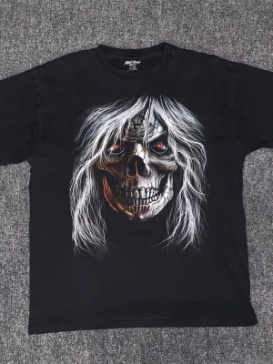 Svart t-shirt med dödskalletryck - Cool svart t-shirt från Kerk Jones med ett stort tryck av en dödskalle med vitt hår och röda ögon på framsidan. Tillverkad i 100% bomull och har en klassisk passform med korta ärmar och rund hals. Perfekt för dig som gillar edgy och unika motiv.