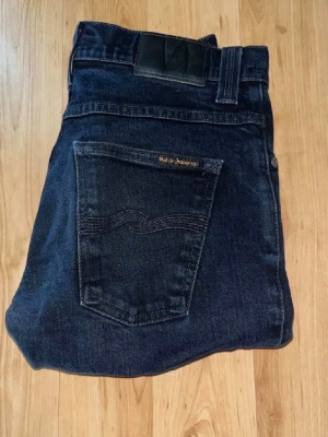 Mörkblå jeans från Nudie Jeans - Snygga mörkblå jeans från Nudie Jeans med klassisk femficksmodell och raka ben. Jeansen har en diskret logga på bakfickan och är tillverkade i slitstark denim. Perfekta för dig som gillar en enkel men stilren look.