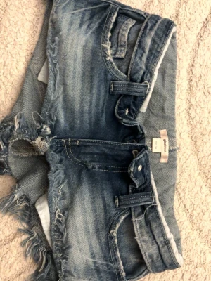 Blå lowaist jeansshorts med fransar - Blå jeansshorts med slitna detaljer och nedvikt kant. Köpt från Gina tricot aldrig använda.