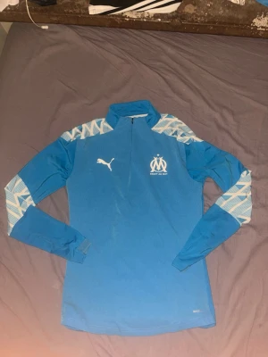 Marseille fotbollskit - Snygg långarmad tränings tröja från säsongen 21/22 för laget OM Marseille, size XS men väldigt stretchigt material, passar S med. Väldigt fint skick andvänd fåtal gånger, inga hål, inga missfärgningar, skriv till mig vid det lilla mista intresset.