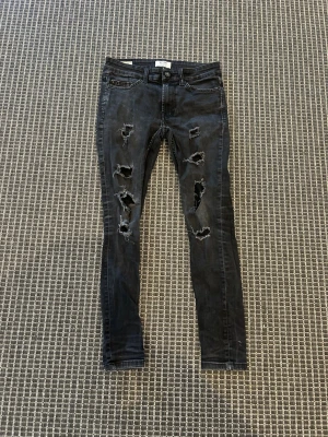 Svarta ripped jeans Only & Sons - Snygga svarta skinny jeans från Only & Sons med slitningar och hål på båda benen. Jeansen har klassisk femficksmodell och knappgylf. Perfekta för en trendig och avslappnad stil.