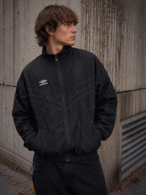 Northern Quarter NQ Relaxed Track Jacket Svart S - Track jacket från Umbros Northern Quarter-kollektion. Inspirerad av klassiska Umbro-arkivplagg med den ikoniska Double Diamond-loggan på bröstet, kontrasterande sömmar och en modern avslappnad silhuett.  Tillverkad i lätt polyester med ventilerande meshfoder för hög komfort. Den boxiga passformen och de grafiska sömdetaljerna ger jackan en tydlig koppling till både fotbollskultur och modern streetwear.