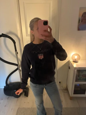 Mörkblå sweatshirt från Gant - Mörkblå sweatshirt från Gant med klassiskt tryck och sköld på bröstet. Tröjan har rund halsringning och ribbade muddar vid ärmslut och nederkant. Perfekt för en avslappnad och stilren look.