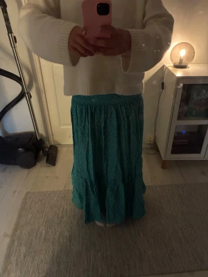 Turkos långkjol med volang - Säljer en turkos långkjol med volangkant och smock i midjan. Kjolen har ett diskret mönster och är gjord i ett lätt, flowy material som passar perfekt till varmare dagar. Superskön och enkel att styla med en stickad tröja eller crop top.
