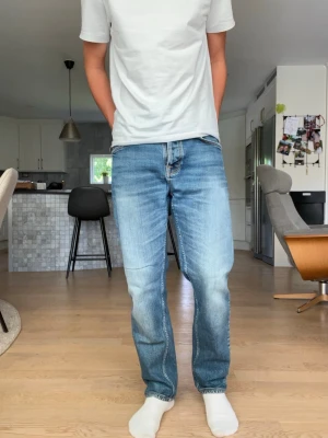 NUDIE JEANS ”STEDDIE EDDIE 2” - Säljer ett par blå jeans med raka ben och snygga slitningar. Jeansen har klassisk femficksdesign och kontrastsömmar på bakfickorna. Tillverkade i denim med en ljus tvätt och avslappnad passform. Perfekta för en casual look. Längd  98 midja 40