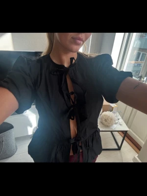 Svart blus, ASOS - Säljer en svart blus med korta puffärmar och flera dekorativa knyt framtill från ASOS. Blusen är aldrig använd och lapparna finns kvar. 🖤