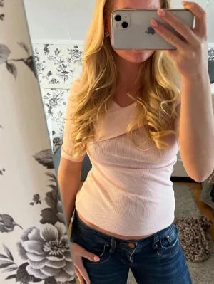 Rosa offshoulder topp - Supersnygg ljusrosa topp med omlottdetalj och ribbad struktur. Toppen har korta ärmar och en v-ringad omlottkrage som ger en trendig look. Perfekt att styla med jeans eller kjol för en fräsch outfit.