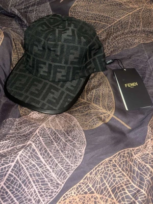 Fendi keps - Snygg svart keps från Fendi med det klassiska FF-monogrammet över hela kepsen. Kepsen har böjd skärm och justerbar rem bak med Fendi-logga. Materialet är textil med detaljer i läderimitation på skärmen. Perfekt accessoar för en trendig streetwear-look.